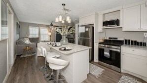 Een moderne keuken met witte kasten, een centraal eiland met barstoelen, roestvrijstalen apparatuur en een hanglamp.