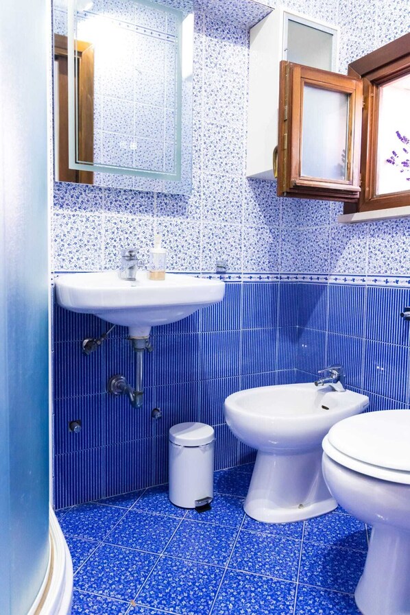 Ein Badezimmer mit Waschbecken, Bidet und Toilette, blau gefliesst mit einem Blumenmuster.