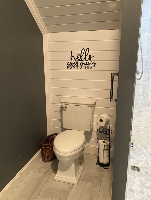 A bathroom with a toilet, a basket, and a toilet paper holder.