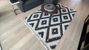 Ein modernes Wohnzimmer mit einem grauen Ecksofa, einem Couchtisch und einem gemusterten Teppich.