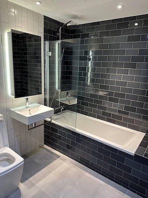 A modern bathroom with a glass-enclosed shower, a white sink, and a toilet. - Immaculate Apartment in London, Royal Docks (London)
