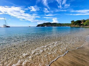 A beach with clear shallow waters, a sailboat, and a distant mountain. - Stunning 3 Bed Villa Overlooking Friendship Bay (Bequia Island)