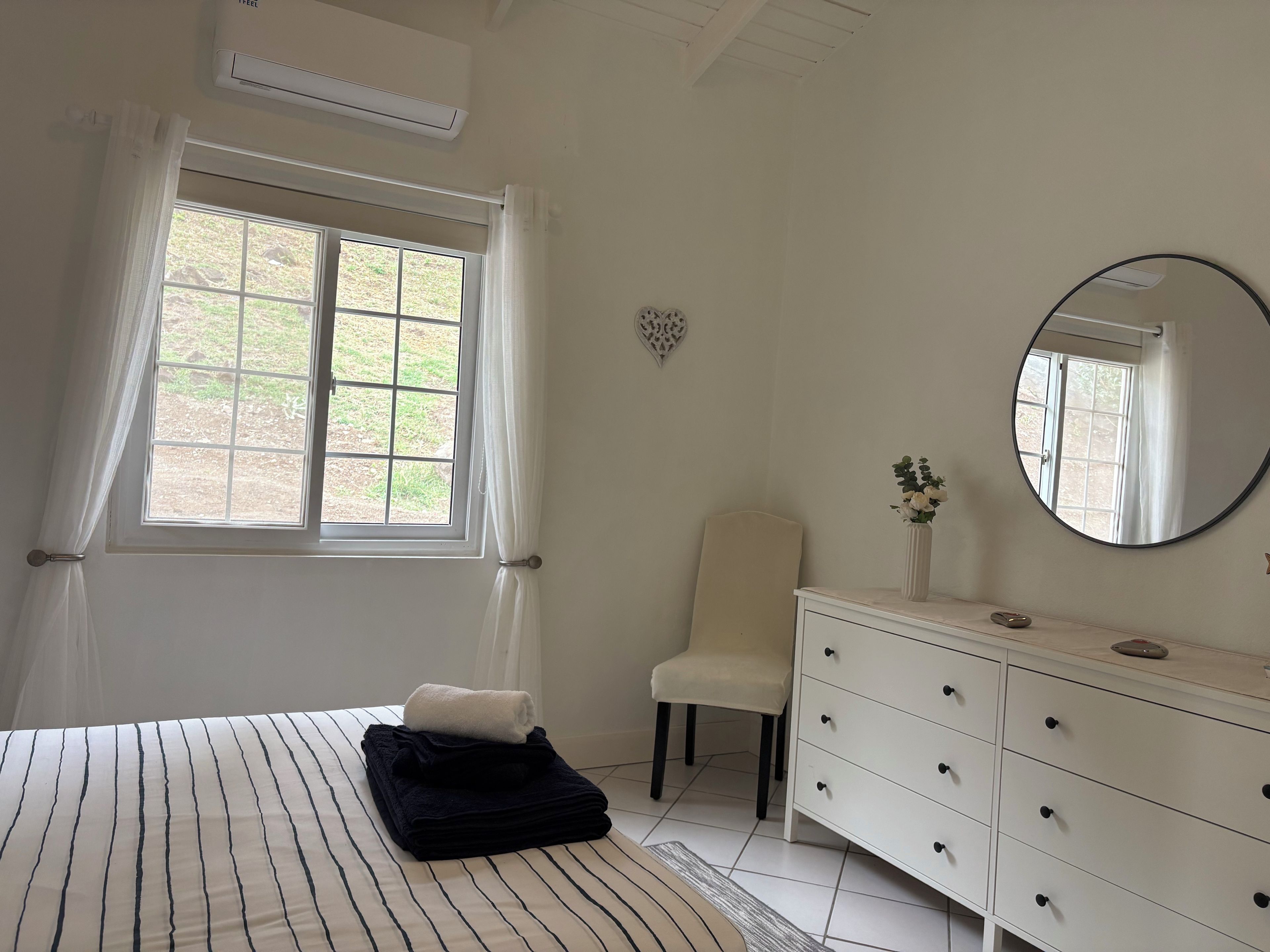 Un dormitorio con cama, una silla, cómoda y ventana con cortinas.