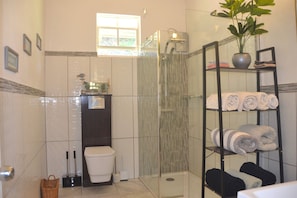 A bathroom with a glass shower enclosure, a toilet, a sink, and a shelf with towels. - Stunning 3 Bed Villa Overlooking Friendship Bay (Bequia Island)