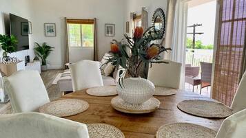 Een eetruimte met een houten tafel, witte stoelen, geweven placematen en een decoratieve vaas met bloemen.