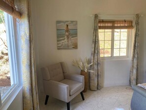 A room with a beige armchair, a painting of a woman by the sea, a window with blinds, and a vase with white flowers. - Stunning 3 Bed Villa Overlooking Friendship Bay (Bequia Island)