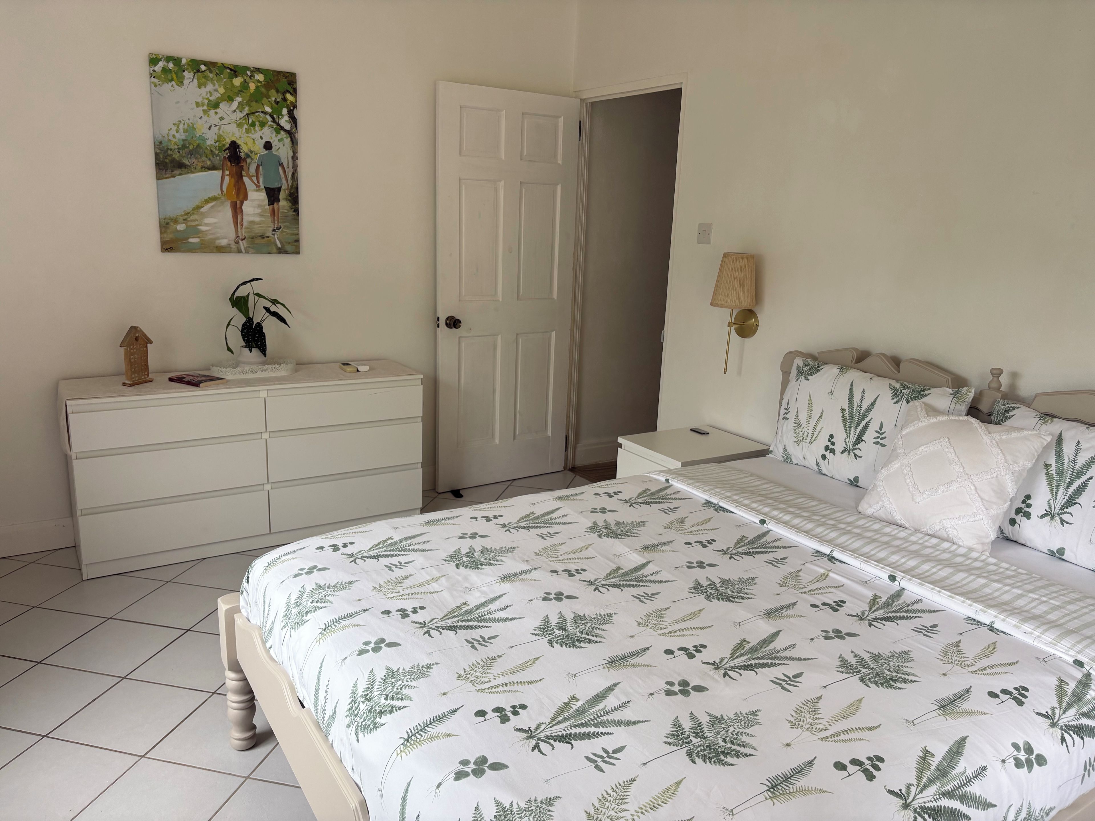 Un dormitorio con cama, cómoda, mesita de noche, lámpara y una puerta.