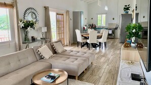 Un grand espace de vie comprenant un canapé, une table basse, une table à manger et des chaises. Au fond, on trouve une cuisine équipée d’un réfrigérateur et d’une cuisinière.