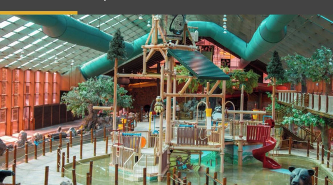 Ein Innenbereich mit einer hölzernen Spielanlage, Rutschen und einem Pool.
