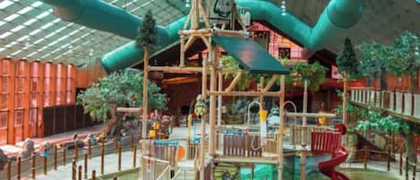 An indoor play area with a wooden play structure, slides, and a pool.
