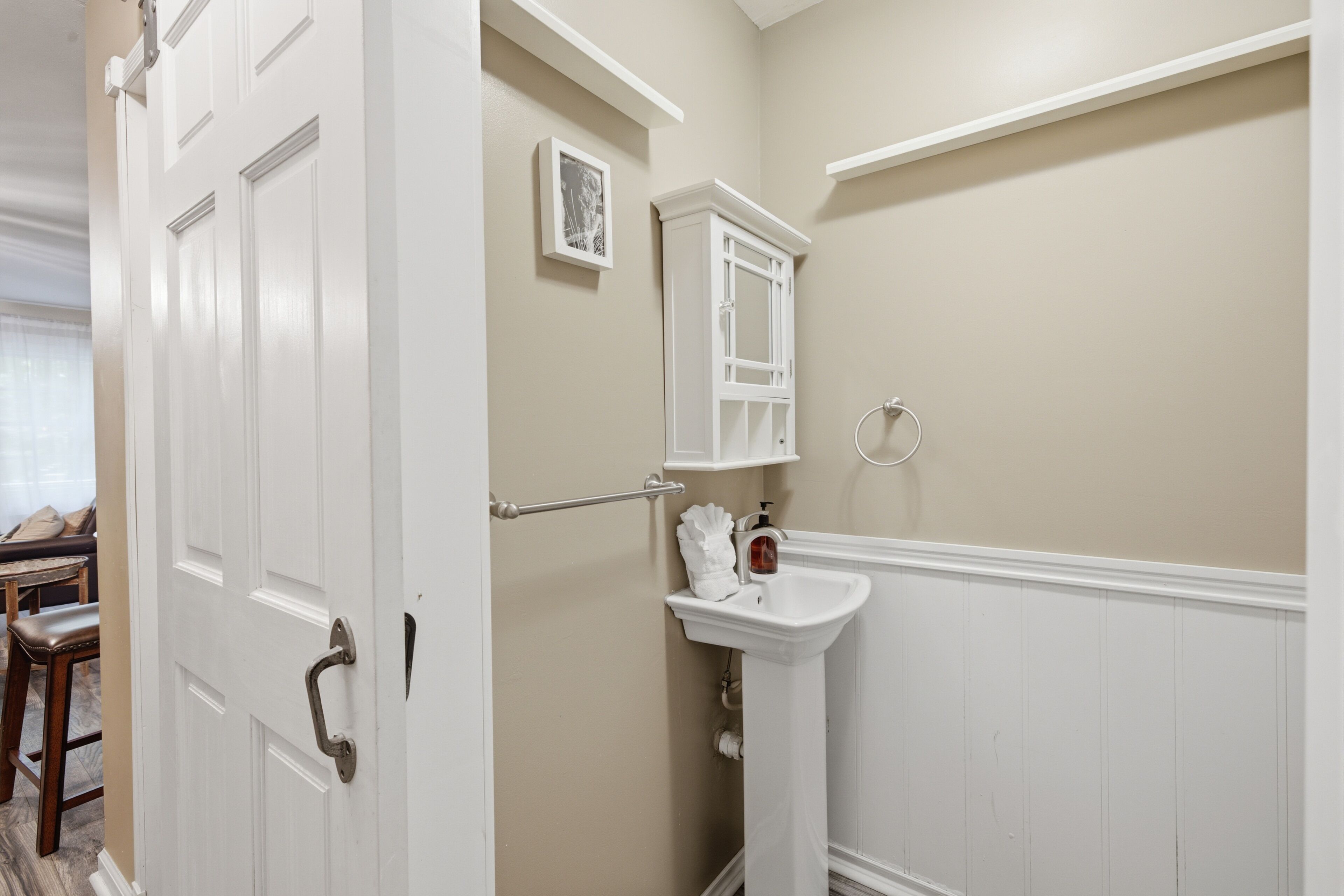 A bathroom with a white door, a sink, a towel rack, and a framed picture on the wall.