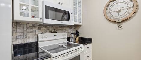 A kitchen with white cabinets, a microwave, a stove, and a clock on the wall.