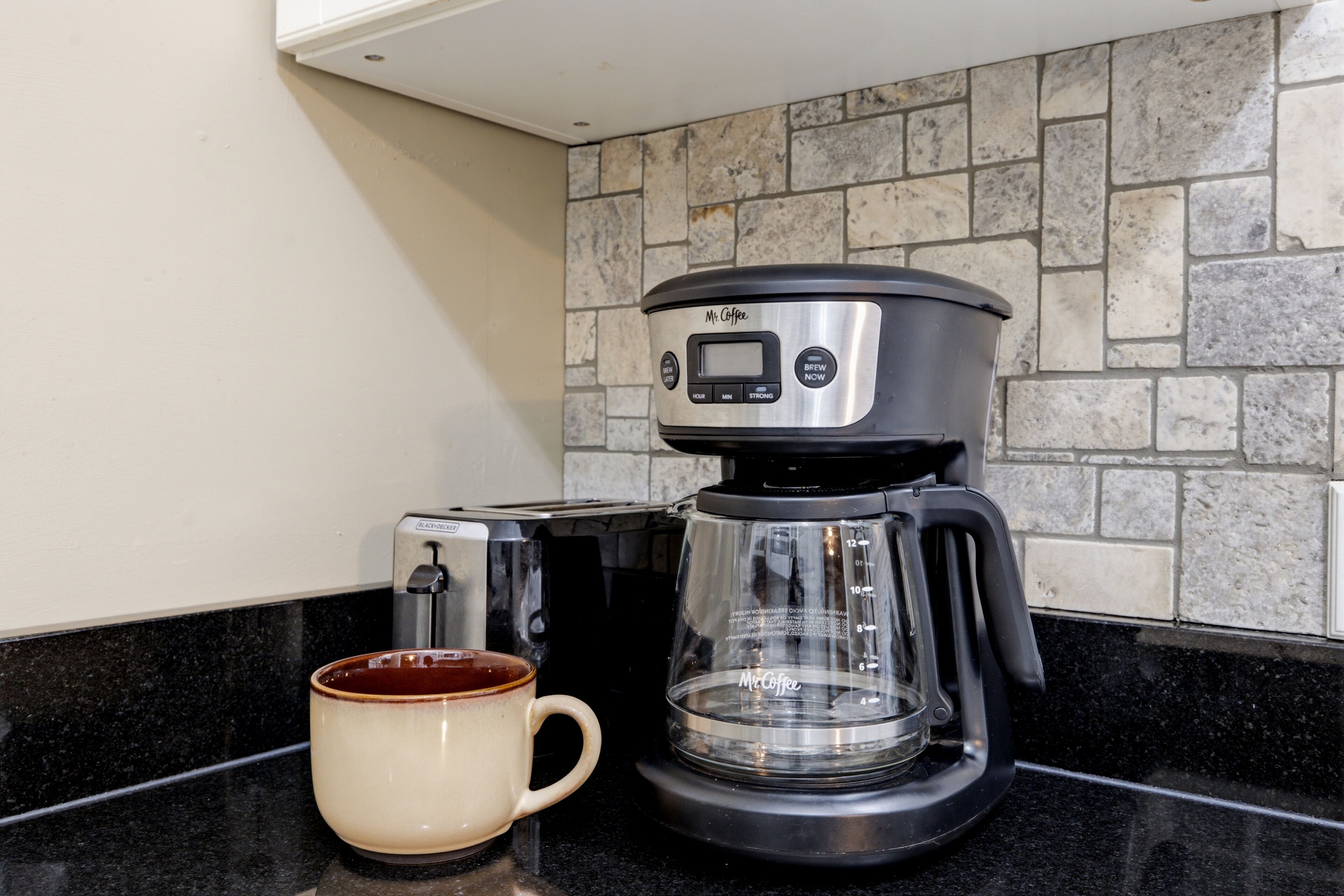 Una cafetera con pantalla digital, una taza y un tostador sobre una encimera de cocina.