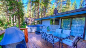 Une terrasse dotée d’une table et de chaises à plateau en verre, entourée de grands arbres.