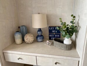 A bedside table with a lamp, a decorative vase, a potted plant, a decorative item, and a sign.