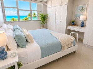 Un dormitorio con cama, escritorio, silla, ventana con vista al océano y una planta en maceta.