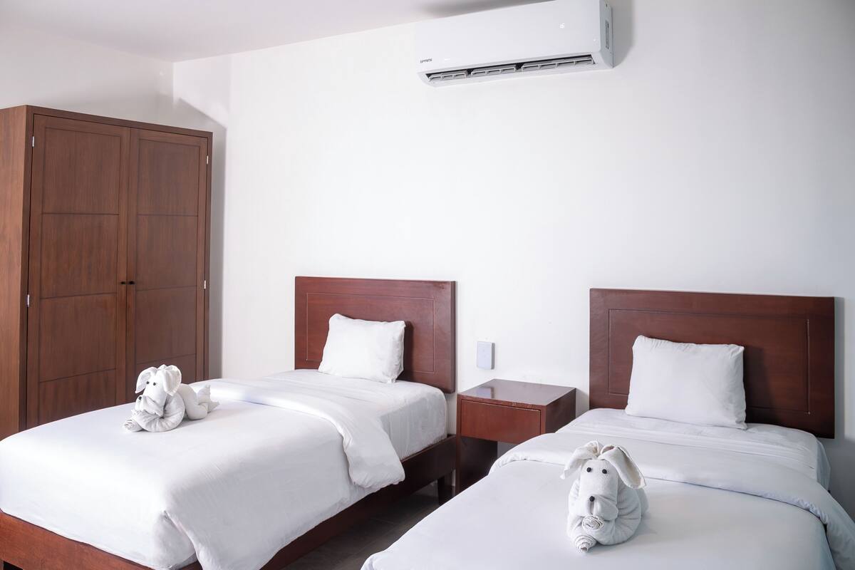 Une chambre d’hôtel avec deux lits, des têtes de lit en bois, du linge de lit blanc et une armoire.
