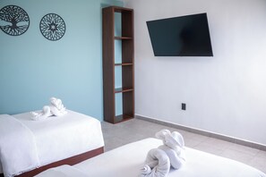 A hotel room with two beds, a TV on the wall, and a wooden shelf unit.