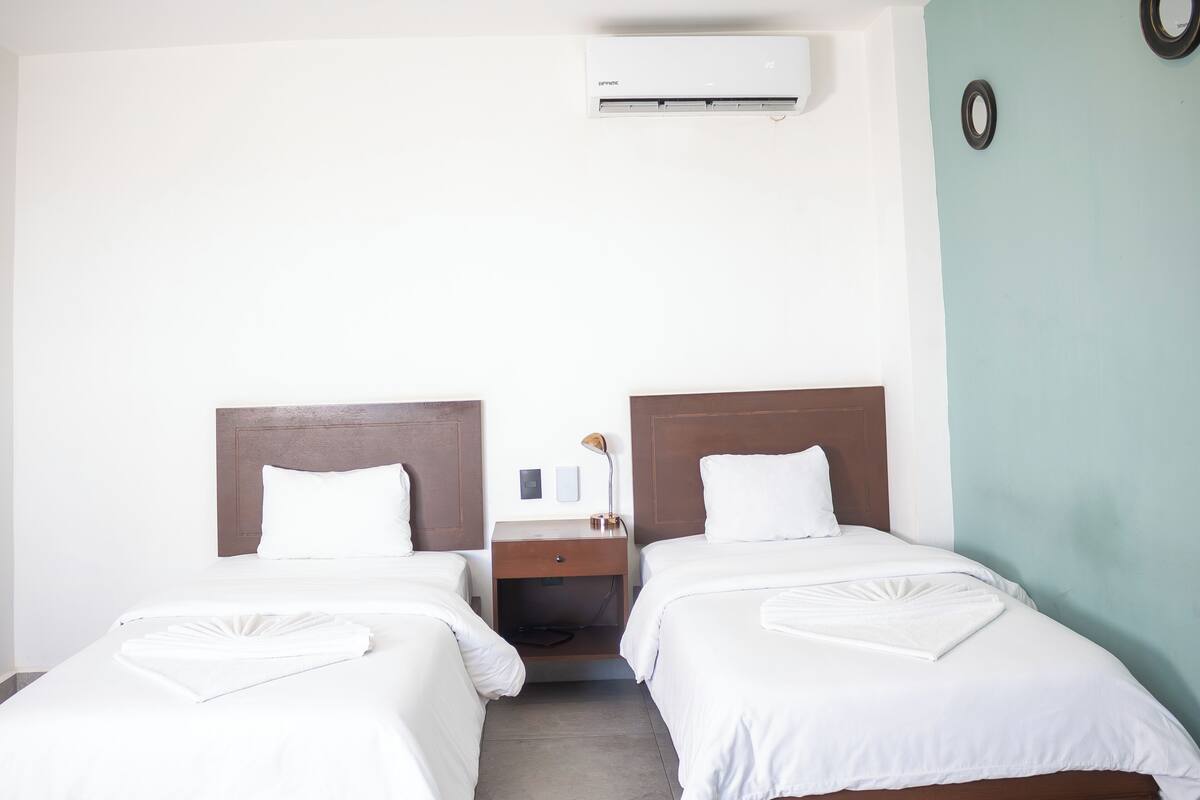 Une chambre d’hôtel avec deux lits, une table de chevet, une lampe et un appareil de climatisation.