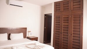 Una habitación de hotel con una cama, una mesita de noche, un aire acondicionado y un armario de madera.