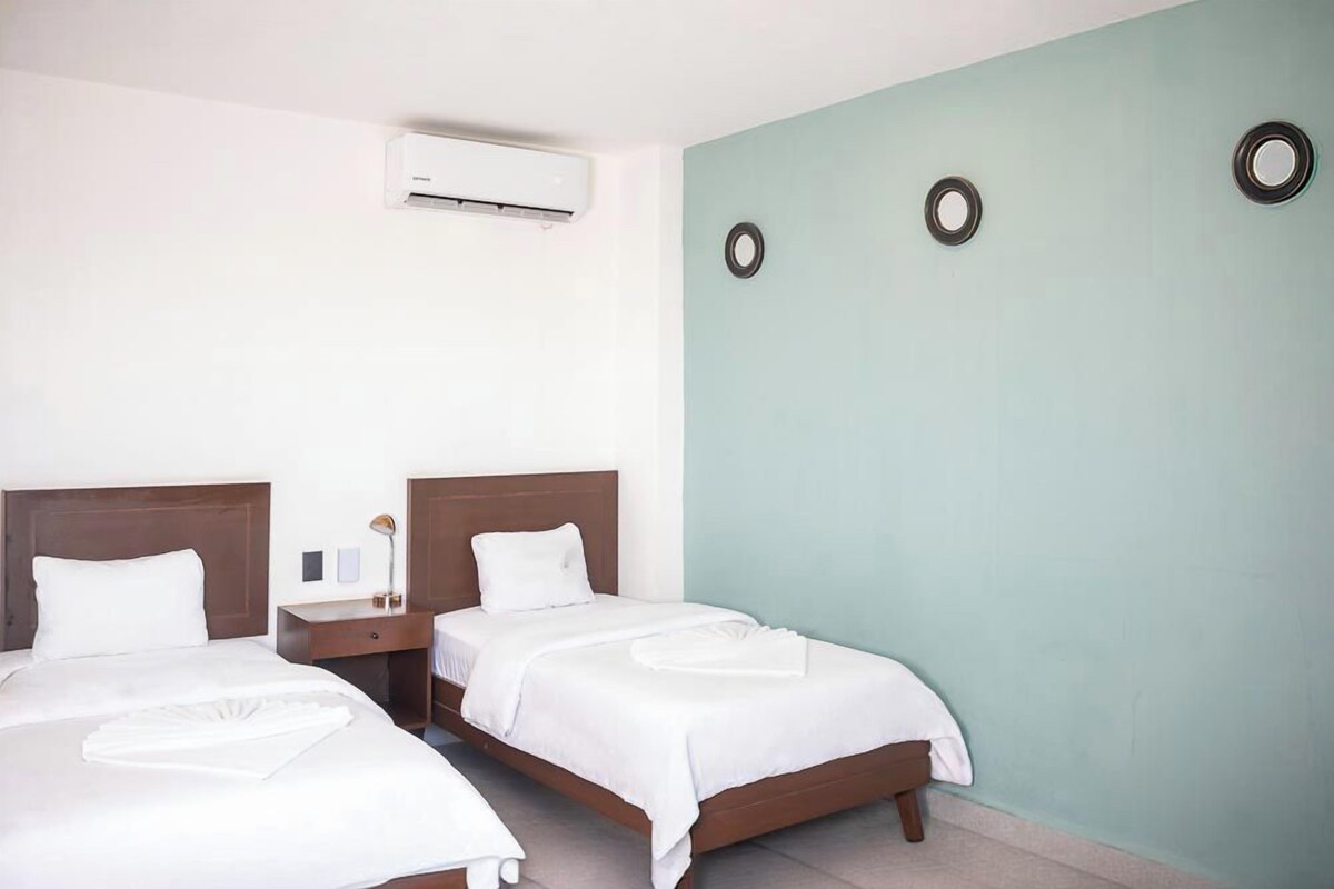 Una habitación de hotel con dos camas, una mesita de noche, una lámpara y un aire acondicionado.