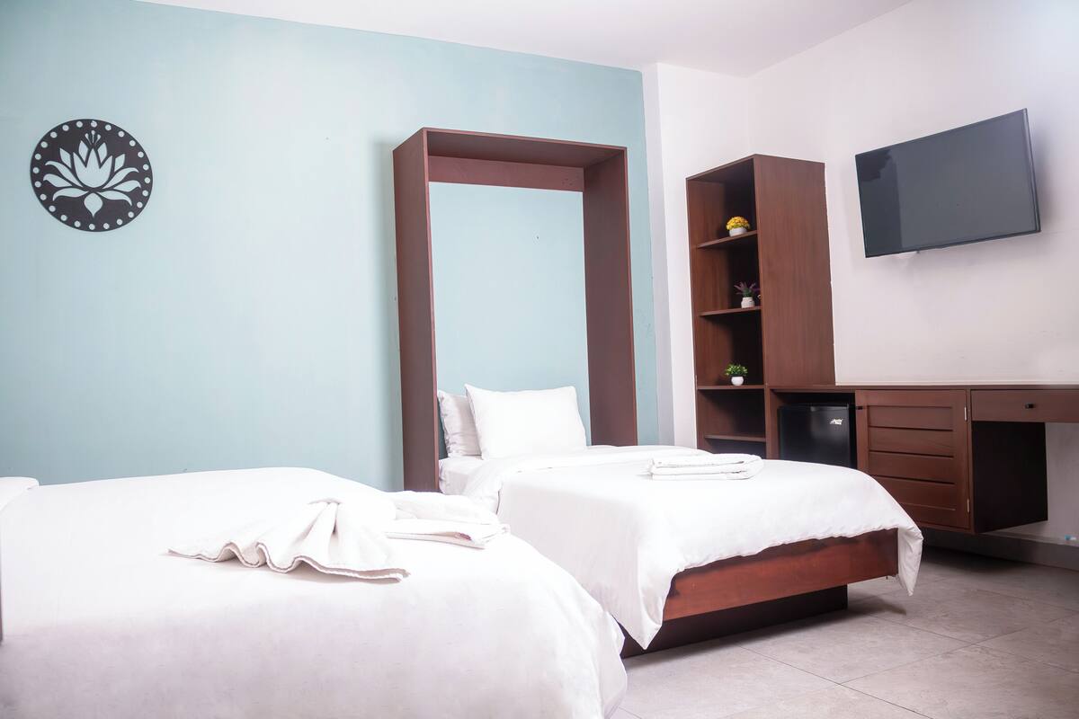 Une chambre d’hôtel avec deux lits, une télévision, une armoire et une petite étagère ornée d’objets décoratifs.