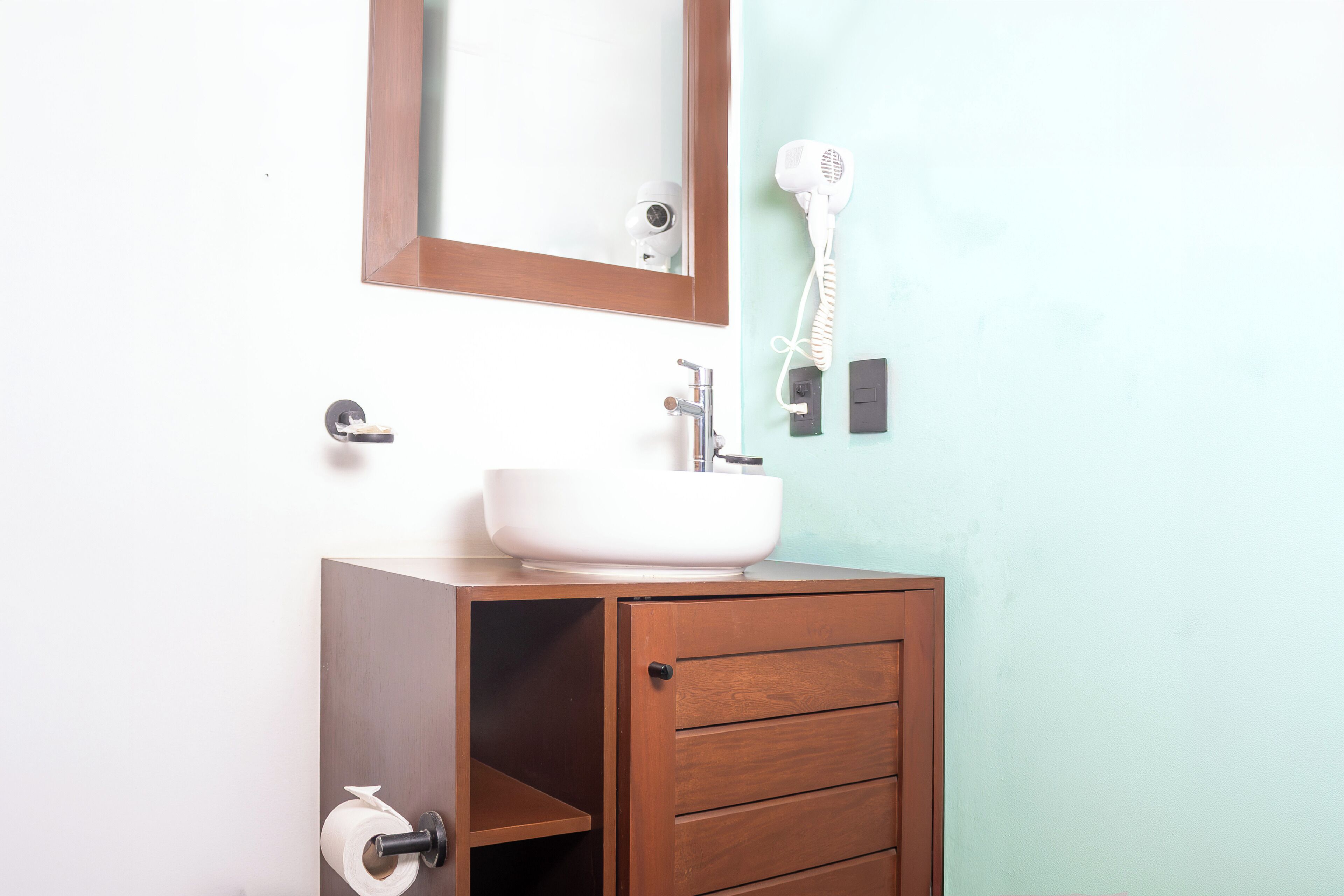Un baño con un armario de madera, un lavabo blanco, un espejo y un secador de pelo montado en la pared.