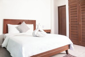 Una cama bien hecha con cabecera de madera, almohada blanca y toalla blanca doblada.
