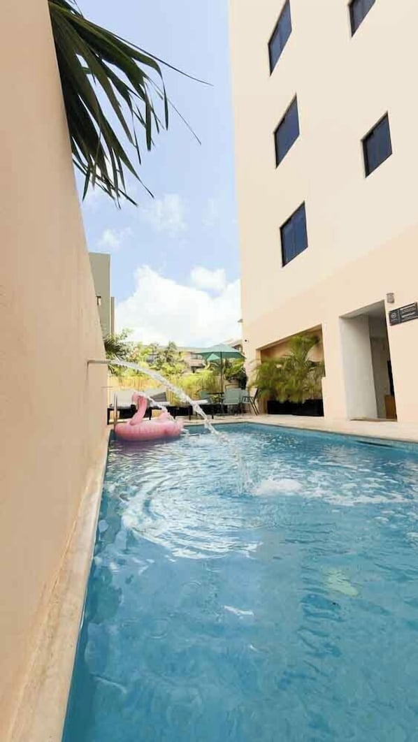 A swimming pool with a pink inflatable flamingo, surrounded by a building with multiple windows.