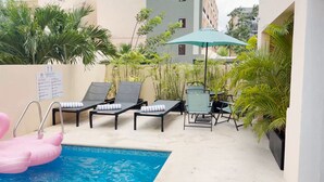 Un área de piscina con sillones de descanso, una mesa y un flotador hinchable rosa.