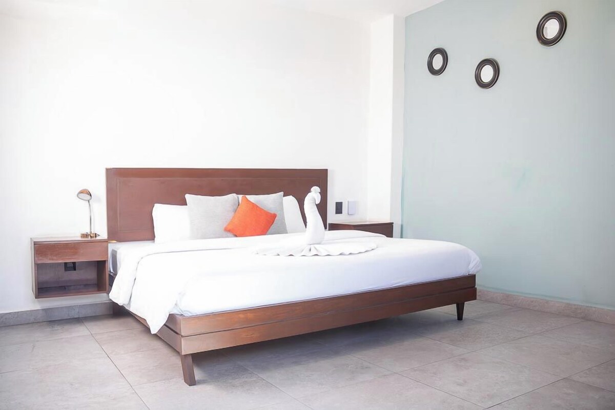 Une chambre d’hôtel moderne avec un lit en bois, du linge de lit blanc et une table de chevet avec une lampe.
