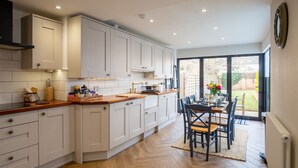 A modern kitchen with white cabinets, a wooden countertop, and a dining area with a table and chairs. - Trinity Cottage, Stratford-upon-Avon - sleeps 5 guests in 3 bedrooms (Stratford-upon-Avon)