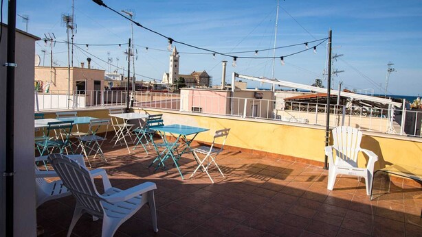 A rooftop terrace with outdoor seating, a view of the sea, and a tower in the background.