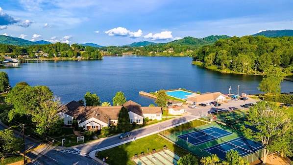 A lakeside property with a tennis court, a swimming pool, and a road leading to a residential area.