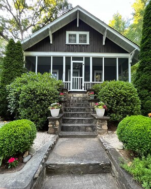 A two-story house with a porch, stone steps, and potted plants.