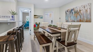 A dining area with a long wooden table and matching chairs, a coffee station with a sign, and a painting on the wall. - Hot Tub~Vilano Beach Serene Walk~parking~2 ACs (St. Augustine)