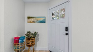 A hallway with a white door, a painting of a beach scene, two wicker baskets with plants, and a patterned rug. - Hot Tub~Vilano Beach Serene Walk~parking~2 ACs (St. Augustine)