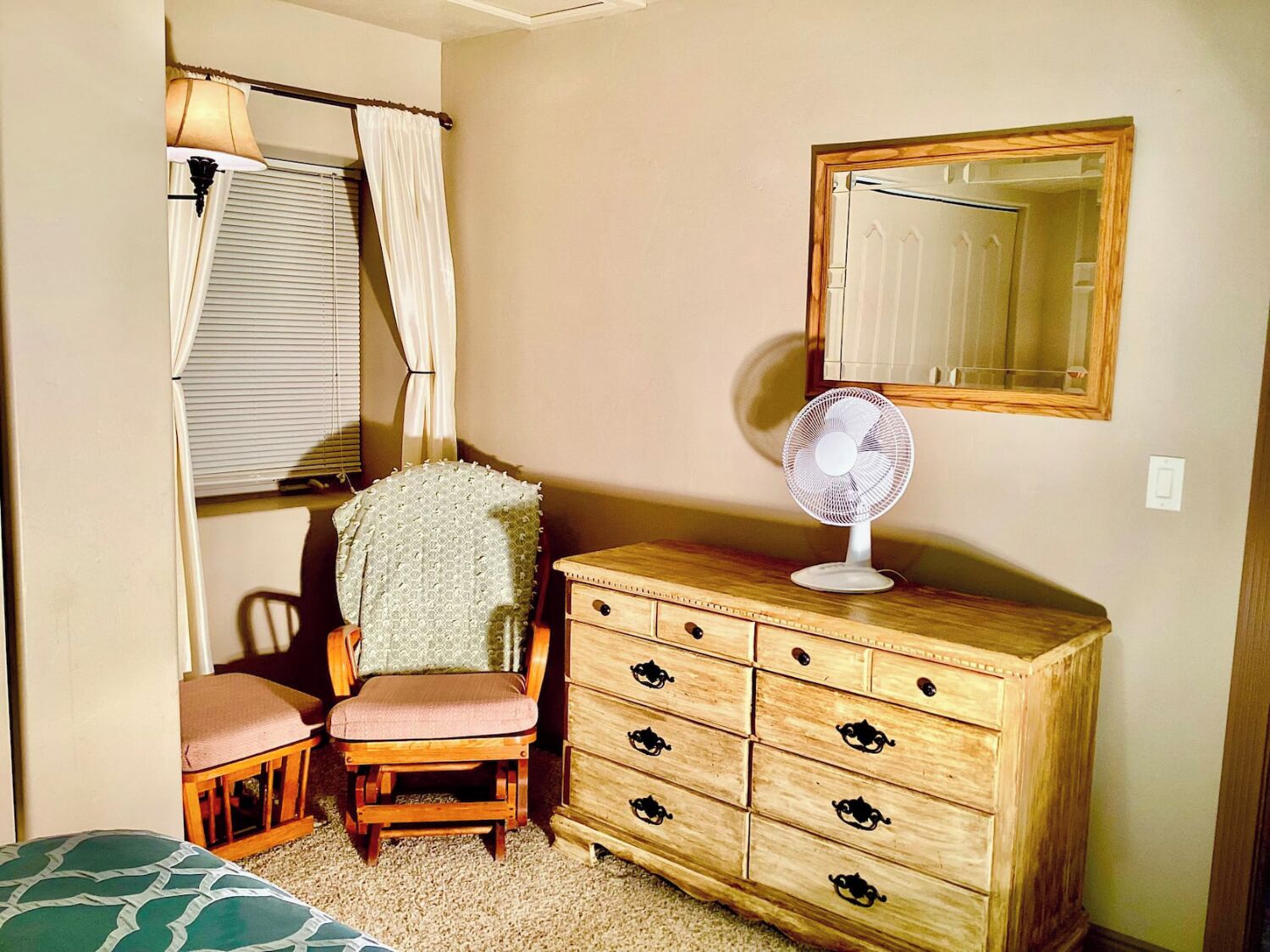 Une chambre avec une commode en bois, une chaise, un lit, une fenêtre avec des rideaux et un miroir au mur.