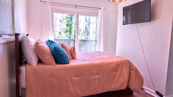 A bedroom with a bed, a TV mounted on the wall, and a window with a view of greenery.