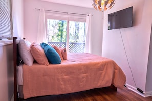 Quarto com cama, televisão na parede e janela com vista para área verde.