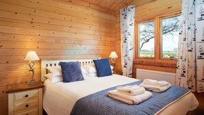 Ein Schlafzimmer mit Holzwänden, einem Bett, zwei Nachttischen und einem Fenster mit Vorhängen.