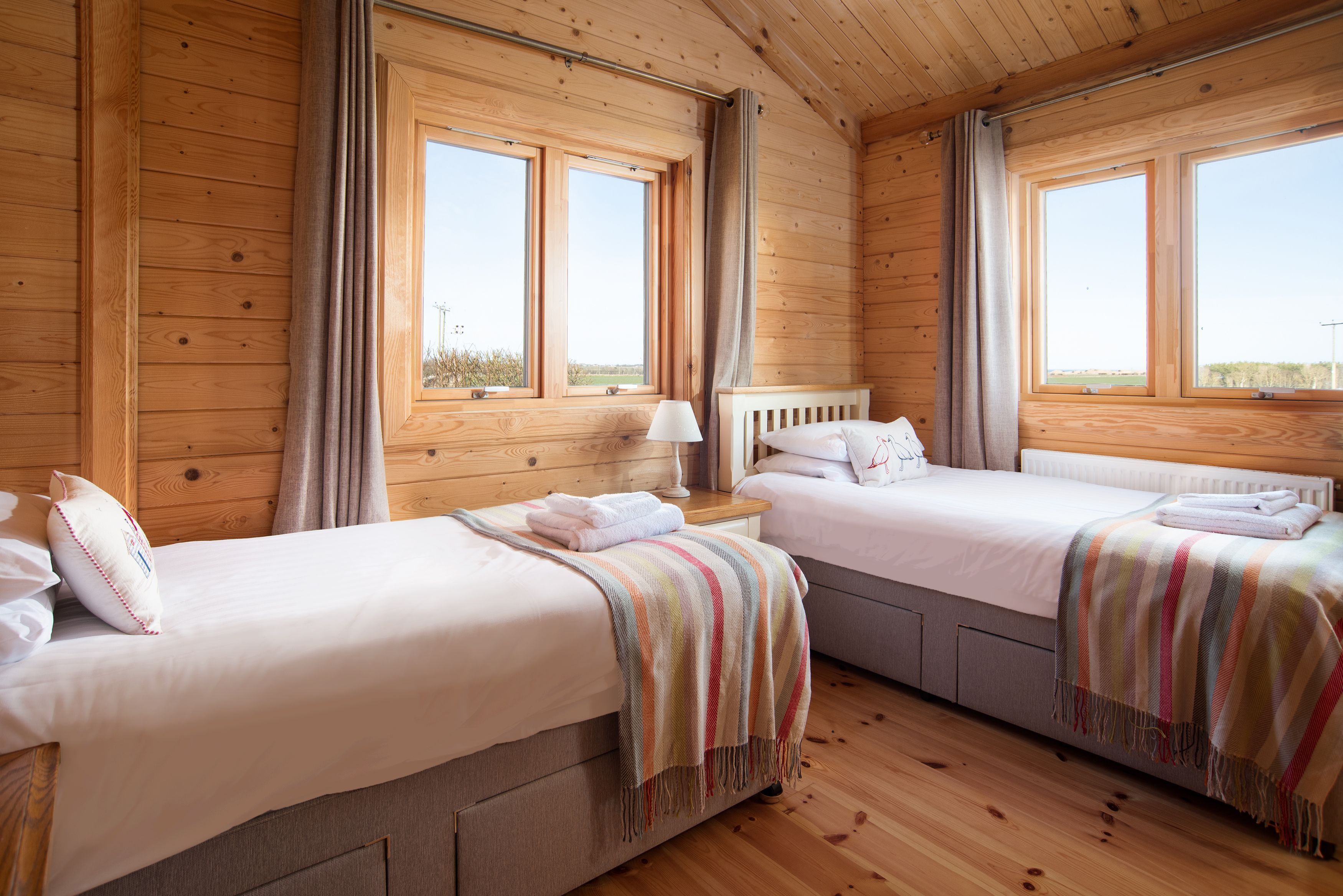 Una camera in una baita di legno con due letti, un comodino e ampie finestre.