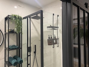 Uma casa de banho moderna com cabine de duche em vidro, prateleiras com toalhas e artigos de higiene pessoal.