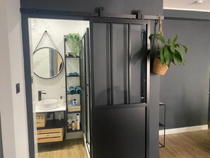 Uma casa de banho moderna com um armário cinzento, um espelho redondo, uma sanita branca e uma prateleira com artigos de higiene pessoal.