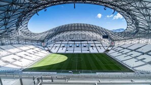 Et stort stadion med buet tagkonstruktion, flere rækker af siddepladser og en central græsbane.