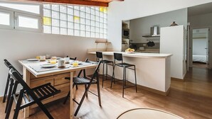 A compact kitchen with a dining area, wooden ceiling, and large windows.