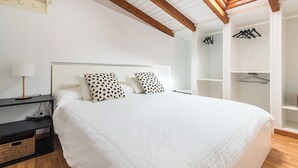 A bedroom with a large bed, a nightstand, a lamp, a wooden ceiling, and a skylight.