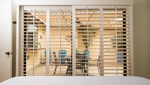 Une chambre avec un lit, une porte blanche et une fenêtre donnant sur une terrasse extérieure aménagée avec une table et des chaises.