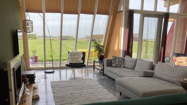 Ein modernes Wohnzimmer mit großem Fenster, einer Couch, einem Sessel und einem Fernseher.