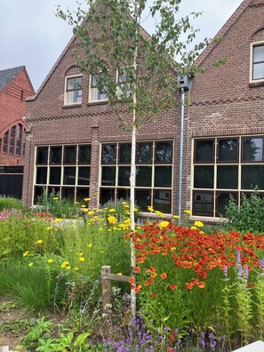 A brick building with large windows and a garden with various flowers.